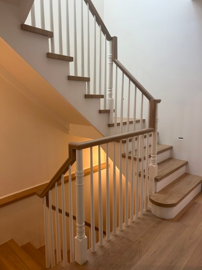 Custom oak staircase with white balusters and wood handrail curving down to a landing
