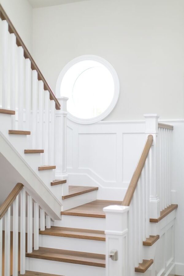 Light wood staircase with white balusters, a matching handrail and a round window.